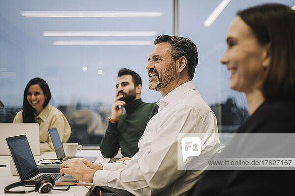 Lächelnder Geschäftsmann  der mit männlichen und weiblichen Kollegen während einer Besprechung im Büro diskutiert