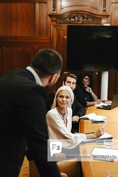 Kollegen schauen auf einen Geschäftsmann  der während einer Sitzung im Sitzungssaal diskutiert