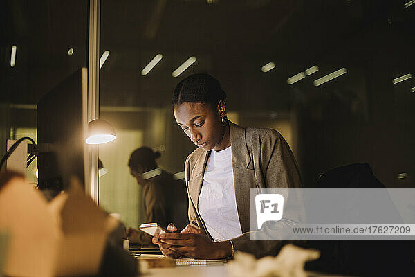 Businesswoman text messaging on smart phone while working in office at night