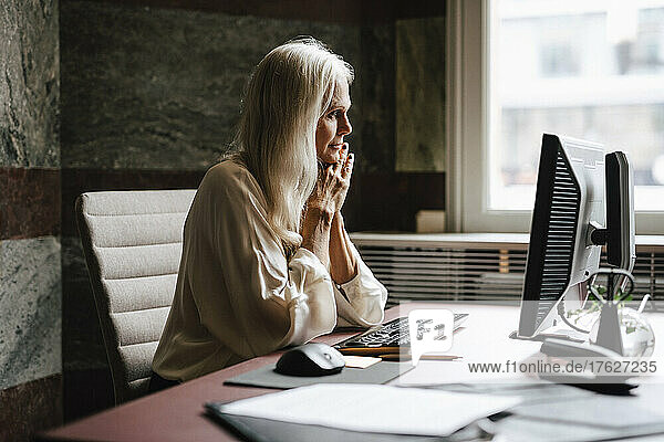 Weibliche Anwältin mit langen weißen Haaren  die im Büro auf einen Computer starrt