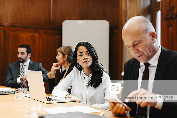Portrait of confident female lawyer in board room with colleagues during meeting