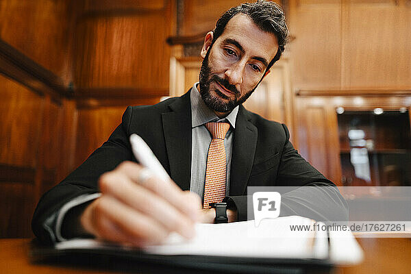 Confident male financial advisor signing contract document in board room during meeting