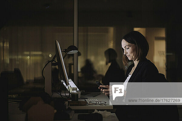 Geschäftsfrau  die ihr Smartphone bei Überstunden am Arbeitsplatz benutzt