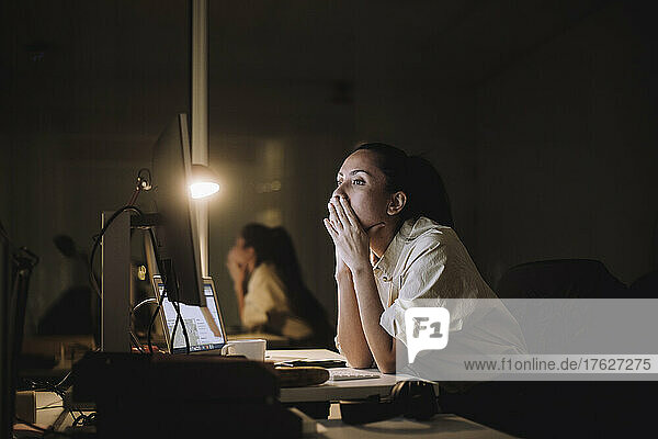 Businesswoman with hands covering mouth working on computer in office