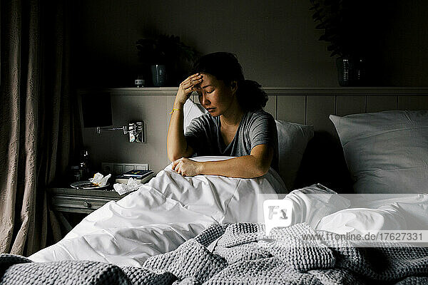 Psychisch depressive Frau sitzt mit dem Kopf in der Hand auf dem Bett zu Hause