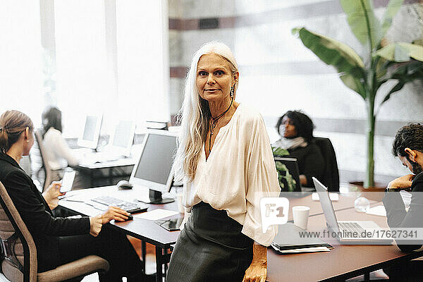 Porträt einer selbstbewussten reifen Geschäftsfrau  die sich im Büro auf den Schreibtisch stützt