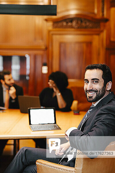 Portrait of smiling bearded male financial advisor sitting at conference table in board room