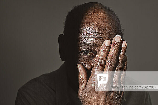 Älterer Mann bedeckt Auge mit Hand im Studio