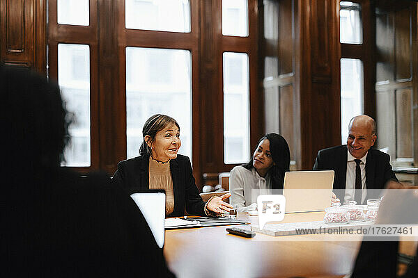 Smiling businesswoman discussing strategy with colleagues in board room at law office