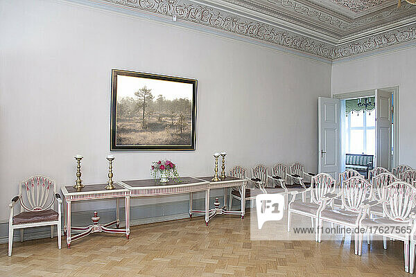 A large room with parquet flooring  elegant chairs and tables.
