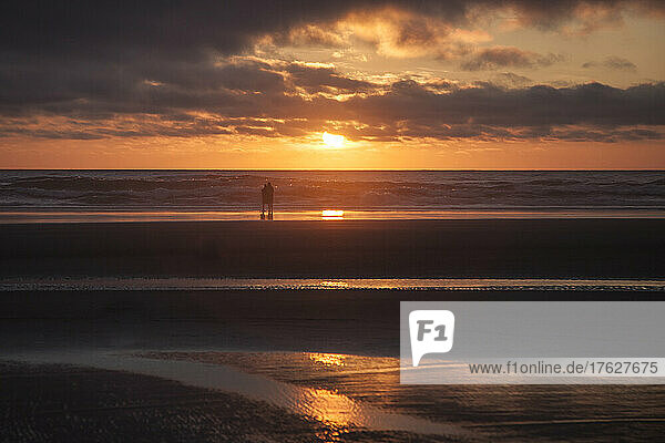 Couple hugging on Cannon Beach with dramatic cloudy sky at sunset.