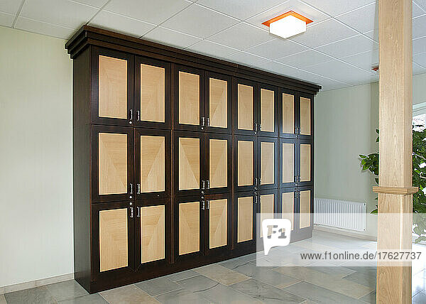 A room with a row of lockers with handles  storage  a tiled floor and ceiling light.