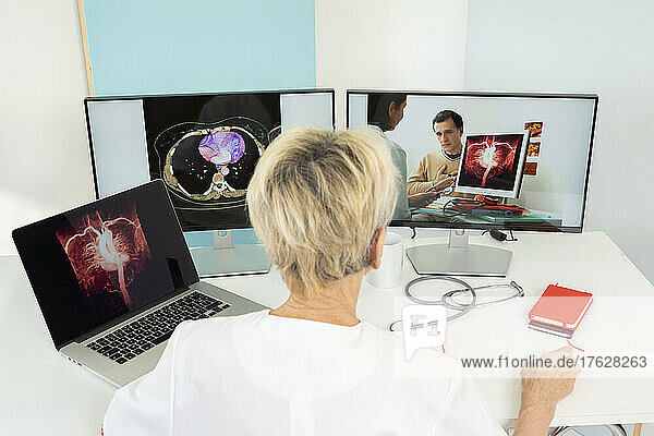 Teleconsultation between two doctors with medical images of hearts on screens.