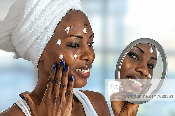 Young girl in front of a bathroom mirror putting cream on a red pimple. Beauty skincare and wellness