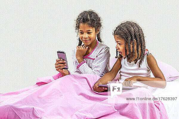 Little girls using digital tablet and smartphone playing in bed.