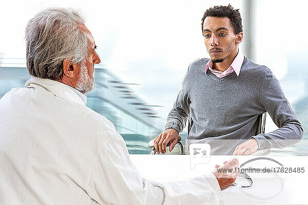 Young male patient having consultation with senior male doctor in medical office.