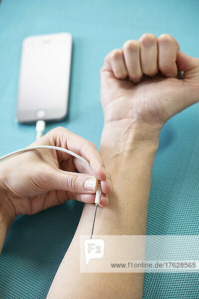 Close-up of a woman's arm giving herself an injection from a smartphone.