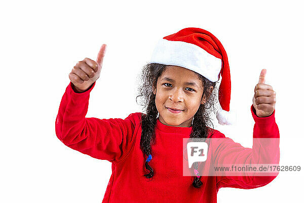 Little girl in a Santa Claus hat shows two thumbs on white background
