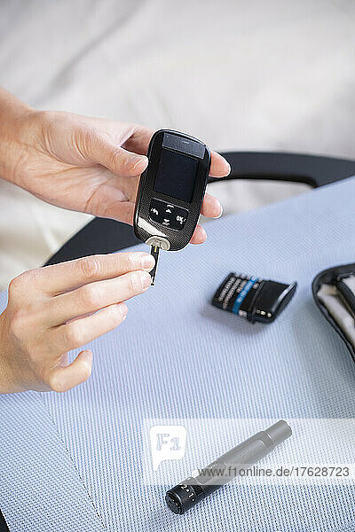 Close-up of the hands of a diabetic woman inserting a tab into a device to measure her blood sugar level.