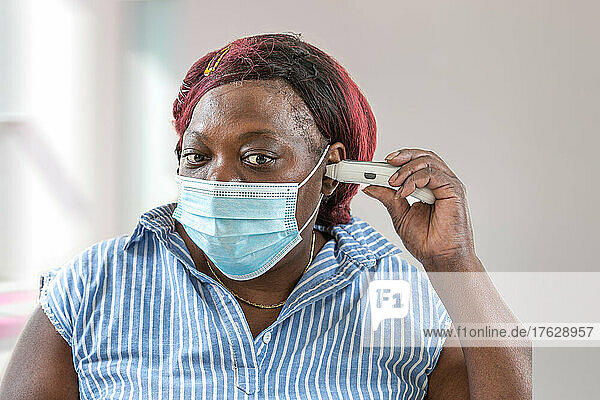 Fever and coronavirus symptoms  woman in medical mask measures body temperature.