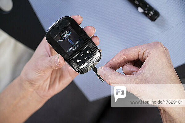 Close-up of the hands of a diabetic woman inserting a tab into a device to measure her blood sugar level.