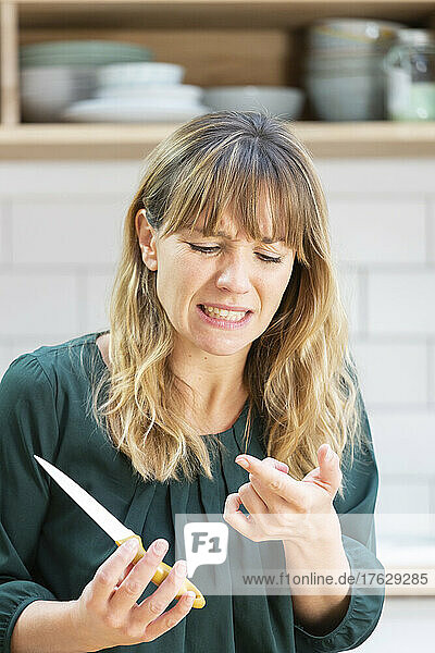 Young woman cutting her finger with a kitchen knife.