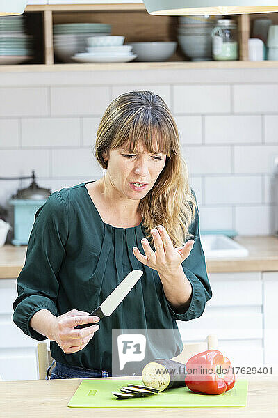 Young woman cutting her finger with a kitchen knife.