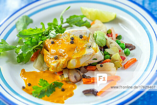 Steamed cod fillet with curry sauce and salad leaves.