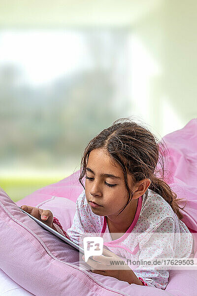 Little girl using digital tablet and playing in bed.
