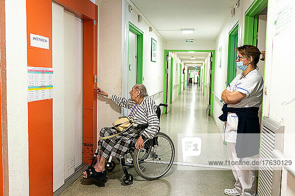 Centenary traveling in a wheelchair  assisted by a nursing assistant in an nursing home.