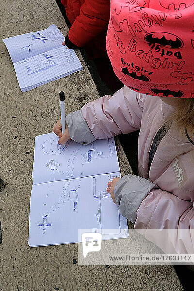 Ukrainian refugees in front of the Embassy of Ukraine - Bucharest - Romania to obtain a biometric passport. Children draw war scenes in their notebooks while waiting to be received at the embassy with their parents.