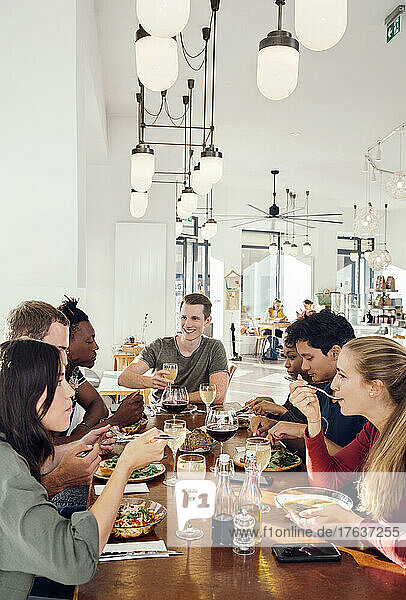 Group of smiling friends enjoying meal in restaurant