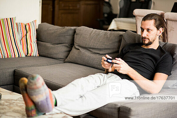 Man on sofa playing video game at home