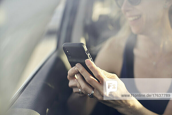 Smiling mature woman using smart phone in car