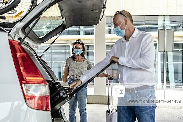 A taxi or Uber driver helping a passenger in a protective mask with her luggage at the airport