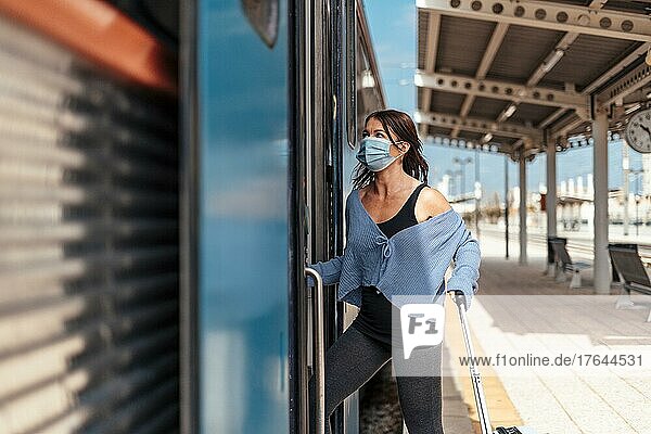 A young woman in protective mask getting on the train with a luggage
