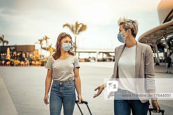 Traveling women in protective masks talking when leaving the airport at their destination