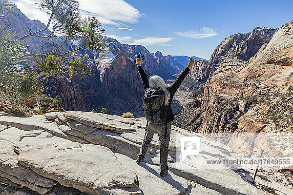 United States  Utah  Zion National Park  Rear view of senior female hiker on Angels Landing trail in Zion National Park Utah with arms raised