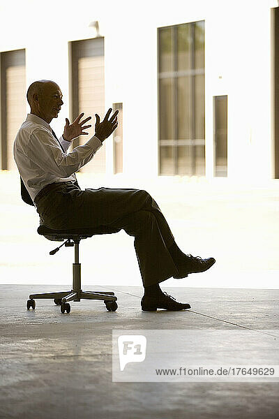 Businessman in warehouse sitting on office chair and gesturing
