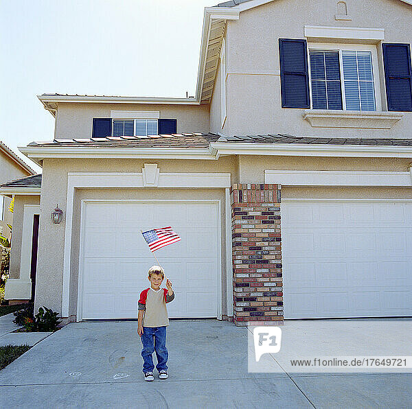 Boy (6-7) waving US flag in front of house
