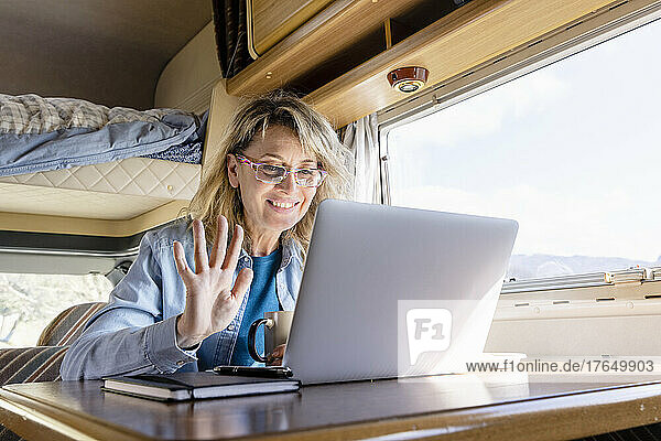 Smiling woman waving on video call over laptop in camper van