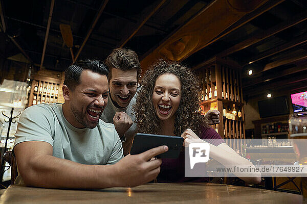 Cheerful soccer fans watching a match on smartphone in a pub