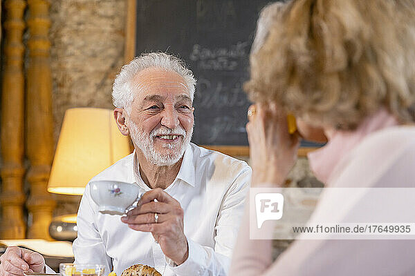 Smiling man holding coffee cup looking at woman sitting in boutique hotel