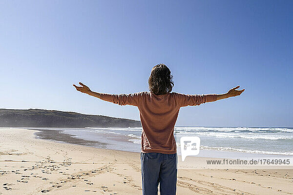 Woman with arms outstretched standing at beach on sunny day
