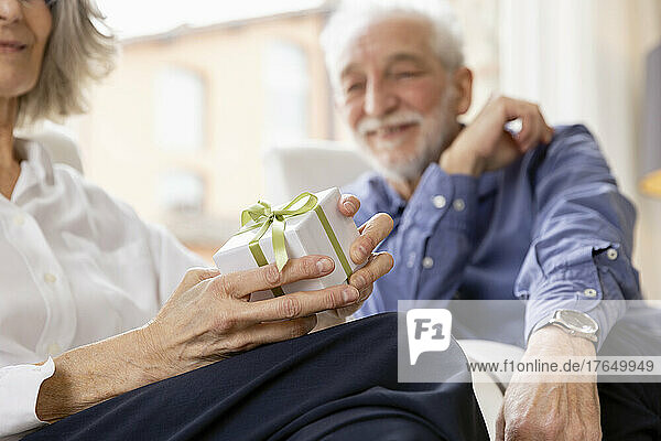 Happy senior woman with gift box sitting by man in hotel apartment