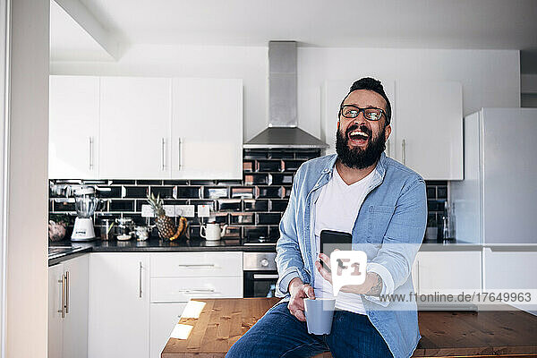 Freelancer with smartphone and coffee cup laughing at home