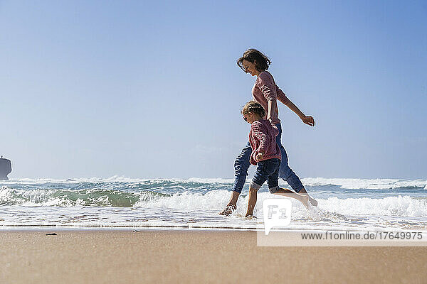 Happy mother and daughter running in water at beach on sunny day