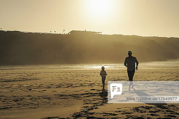 Father with daughter running on beach at sunset