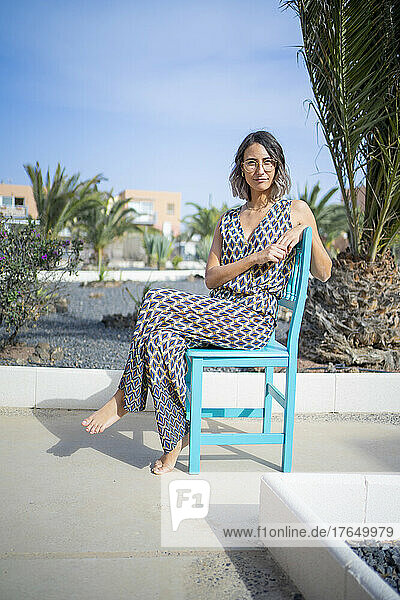 Junge Frau sitzt an einem sonnigen Tag auf einem blauen Stuhl