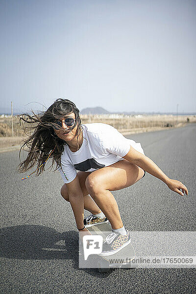 Woman with tousled hair skateboarding on sunny day